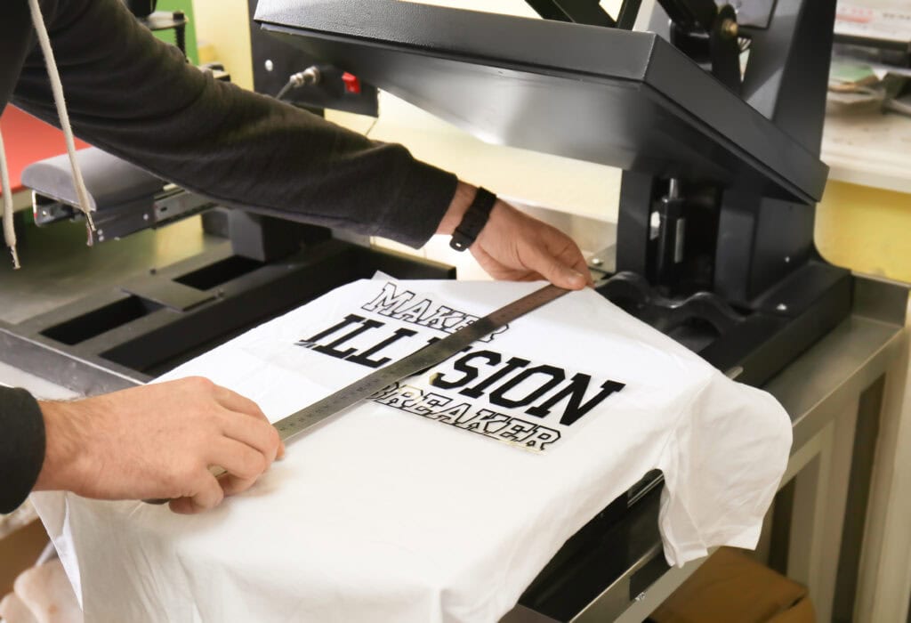 Young man printing on t-shirt at workshop